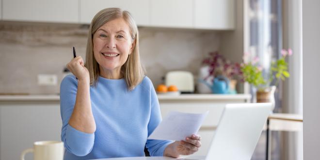 Middle-aged woman working happily in front of a computer in her kitchen.