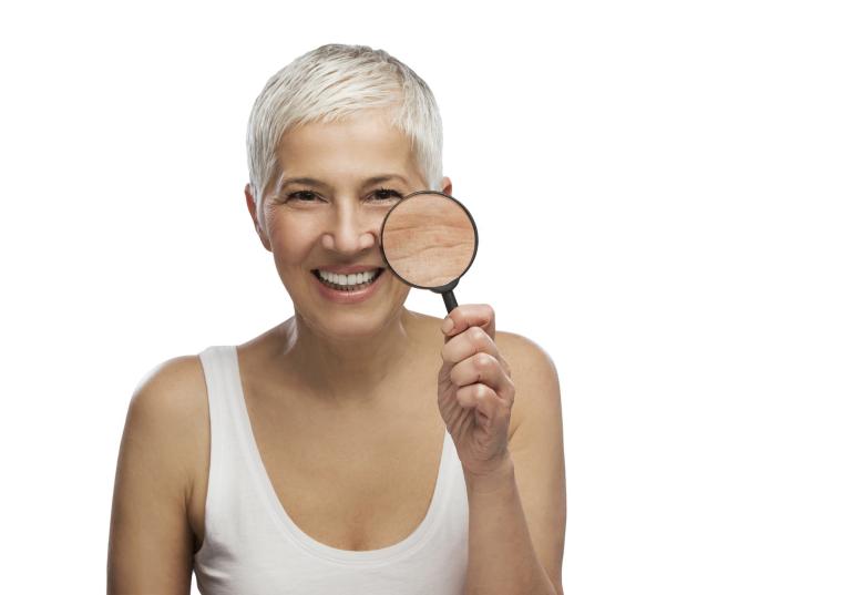 White middle-aged woman with short white hair holding a magnifying glass to her cheek.